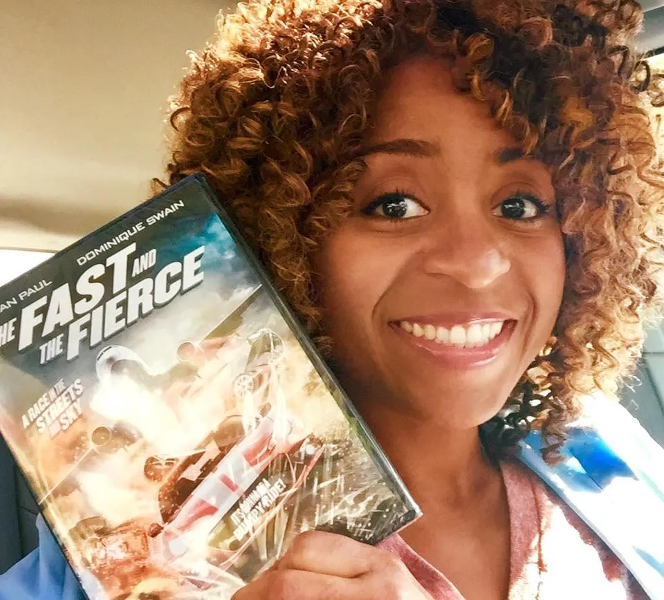 A smiling woman with curly hair holds up the DVD of The Asylum’s The Fast and the Fierce.