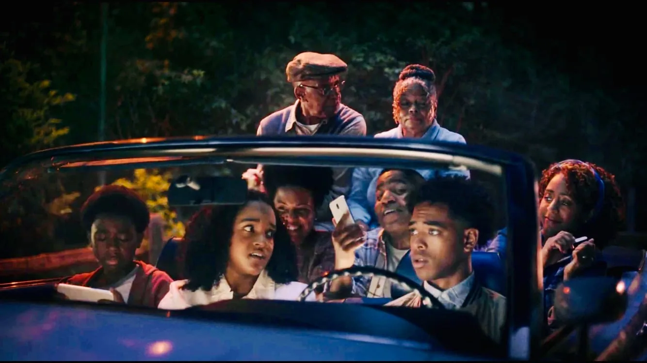 Still from the Boost Mobile commercial: a family crowded into a blue convertible at night, several looking at phones, two elders standing in back