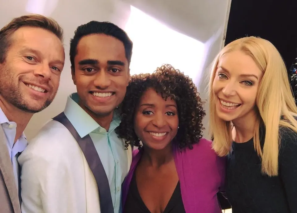 Group selfie from the Brightside shoot of four smiling people on a set: two men and two women, one woman in a purple cardigan.