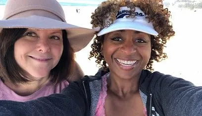 Two women smiling in a beach selfie, one in a wide-brimmed hat and one in a white visor, at the first beach meeting for How Comedy Landed Me in the Psych Ward