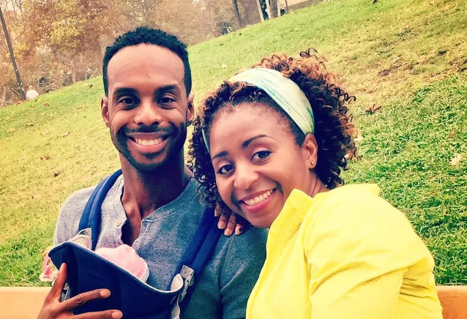 Sophia Thomas as Janet, in a yellow jacket and headband, with Lawrence Stallings and a baby in a carrier on a park bench, on set for the series