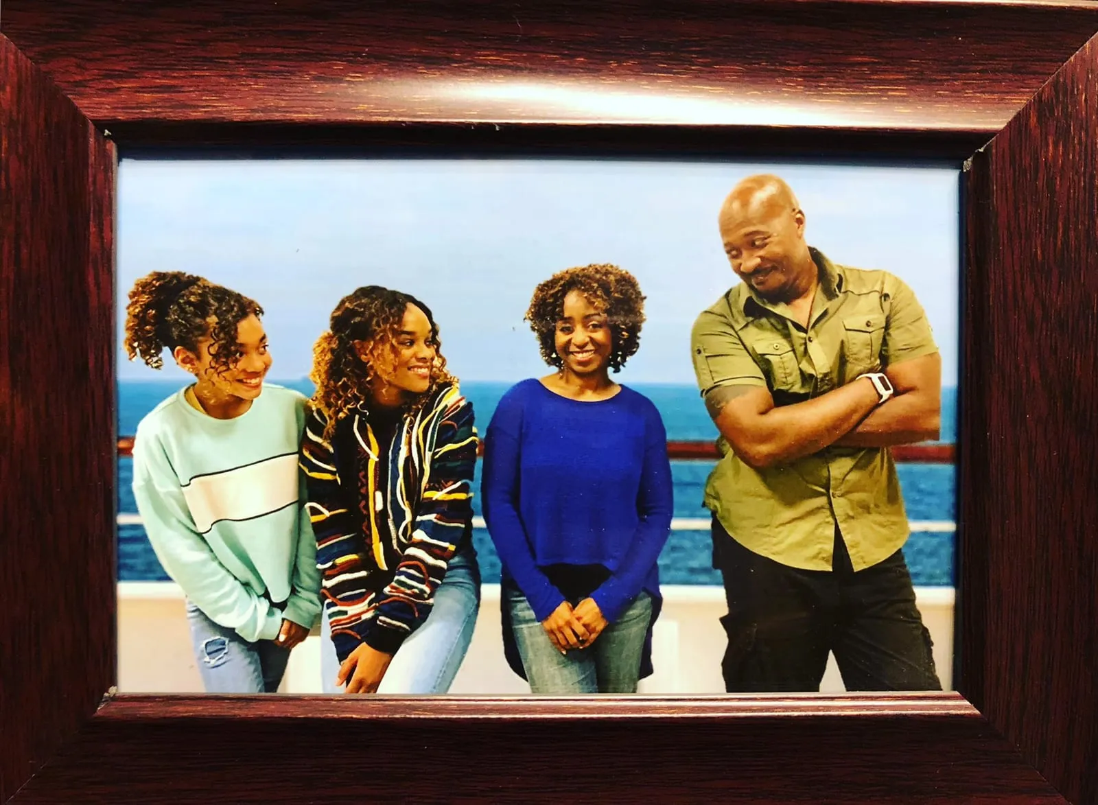 Framed photo of Sophia Thomas as Kate with her film family on the set of HOME, posed against an ocean railing