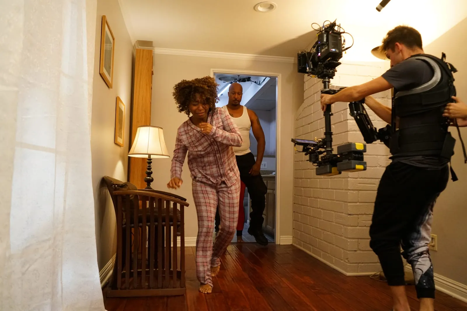 Behind the scenes of HOME: Sophia Thomas as Kate runs barefoot in plaid pajamas, a man behind her, as an operator films with a stabilized camera rig.