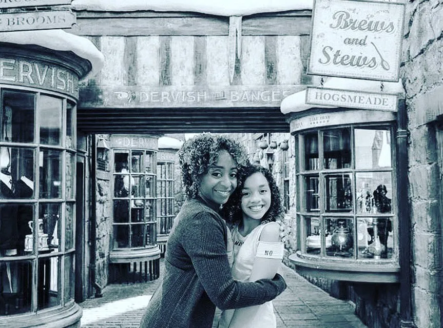 Black-and-white photo of Sophia Thomas and Amara Rose, who play mother and daughter in HOME, hugging on a Hogsmeade-style street.