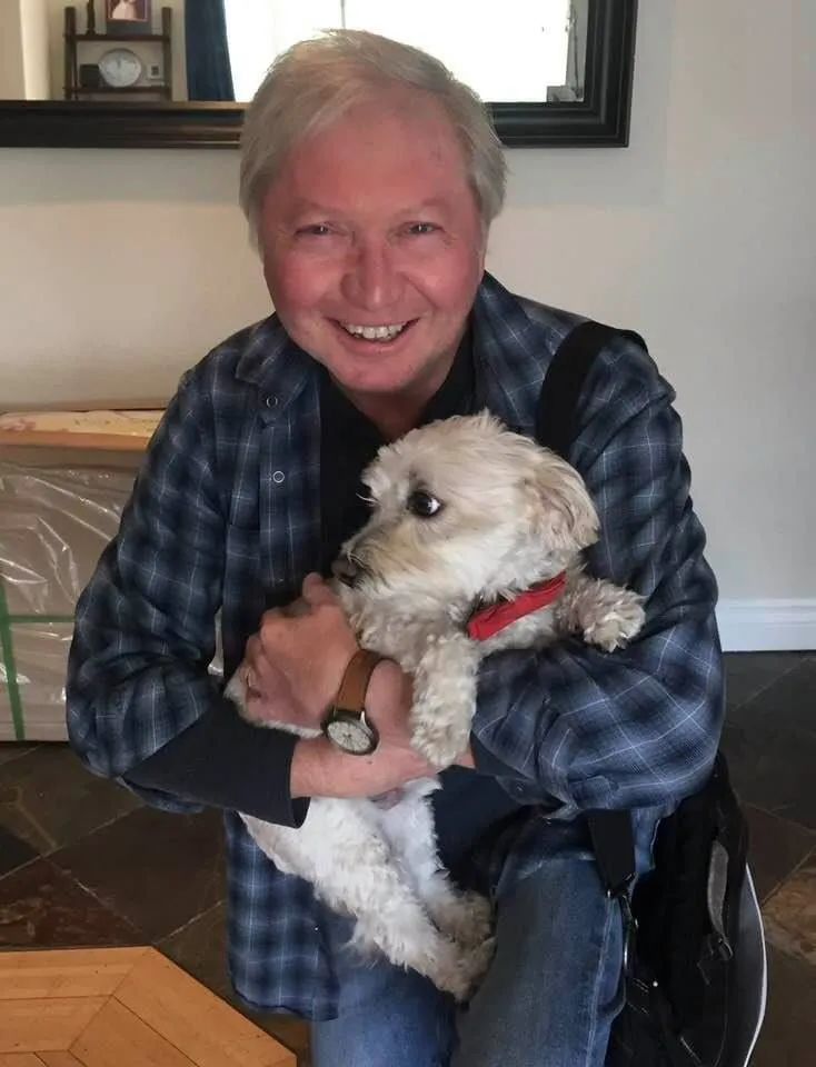 Warren Sweeney smiling as he holds Wilbur Wigglebutt, the small white dog who plays Willie in How Comedy Landed Me in the Psych Ward