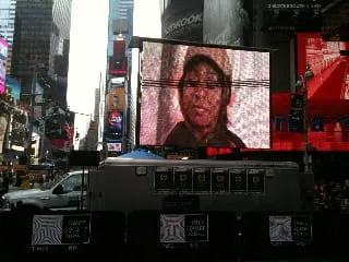 Close view of the Times Square outdoor video screen showing a person in a cap with scan lines at The Visitor’s festival premiere