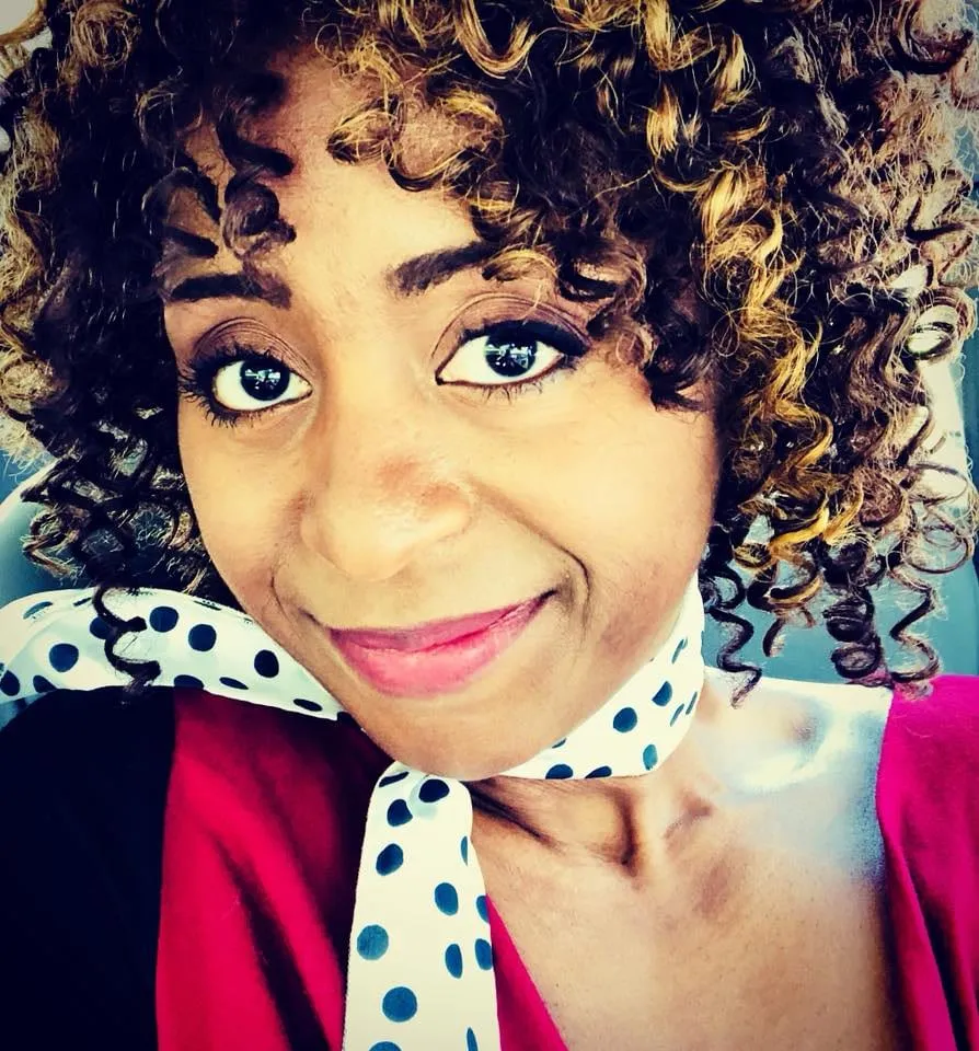Promo selfie for the It’s a Date booking: a smiling woman with curly, honey-highlighted hair, a navy polka-dot scarf and a magenta top.