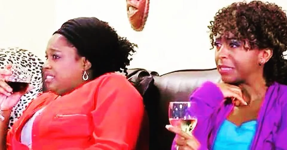 Still from the book club scene in Just Jackie season 2, episode 6: two women on a couch hold wine glasses and wince; Sophia Thomas plays Susan.