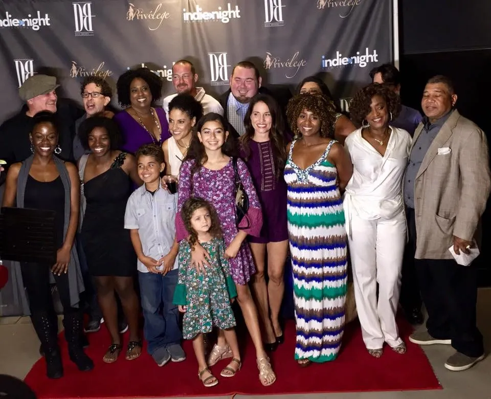 The Just Jackie cast and guests, adults and children, pose together on a red carpet in front of the Indie Night Film Festival backdrop