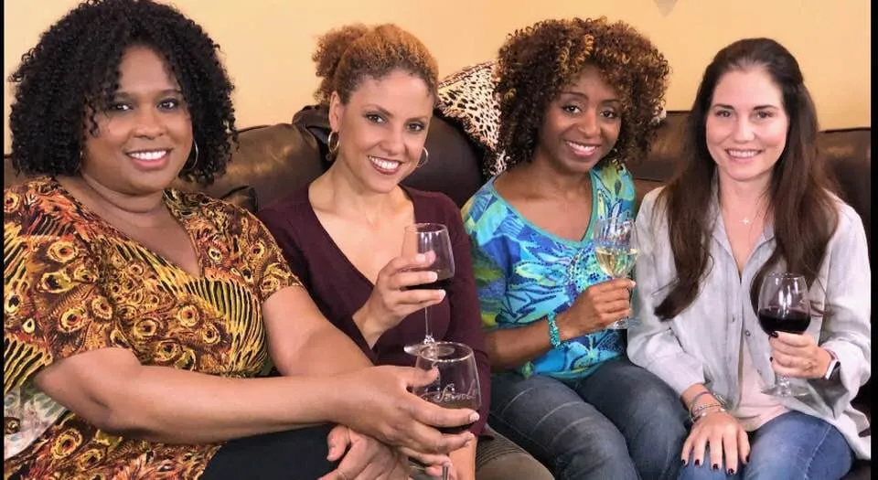 The four bookclub ladies of Just Jackie TV season 2 seated on a leather couch with glasses of wine, smiling at the camera