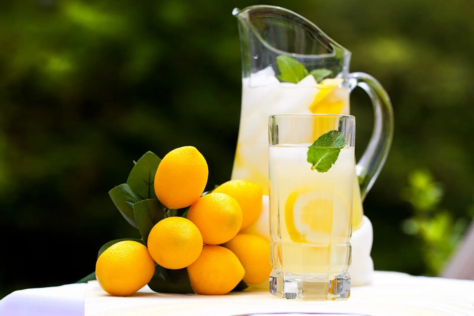 Illustrating turning lemons into lemonade: a pitcher and glass of iced lemonade with mint beside a bunch of fresh lemons.