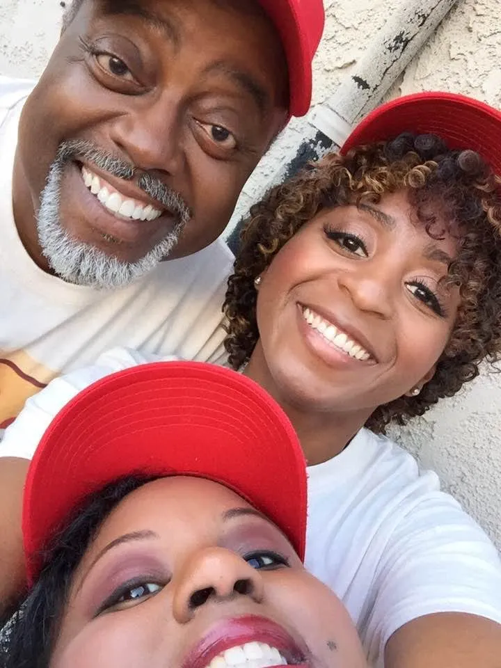 Selfie of three smiling people in red caps and white T-shirts, a gray-bearded man and two women, during the My Name Is Lamar shoot.