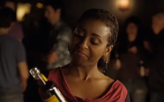 Still from the Newcastle Shooters commercial: a woman in a red top examines a bottle of amber drink in a dim bar.