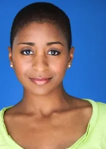 Headshot of Sophia Thomas with closely cropped hair and a lime-green top against a bright blue backdrop, shown as a featured Growing Out Your Hair model.