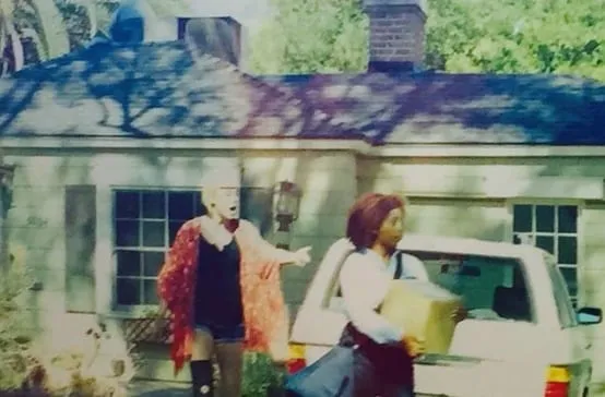 Screen grab from The Other Wife: a woman carrying a package beside a white SUV as a woman in a red cardigan gestures from a house yard
