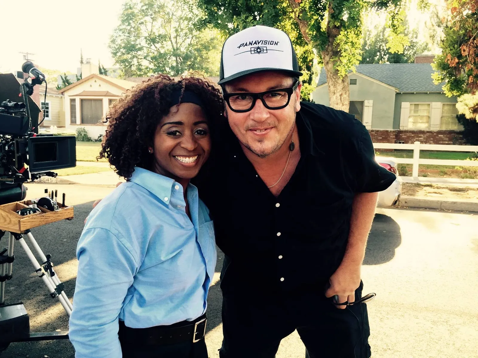 On set of The Other Wife, a smiling woman in a light blue uniform shirt poses beside director Nick Lyon, who wears a Panavision cap and glasses