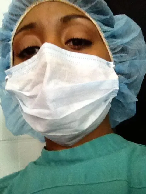 Nurse Whitacker, played by Sophia Thomas in Vicious, in a blue surgical cap, white mask and green scrubs with her eyes cast down